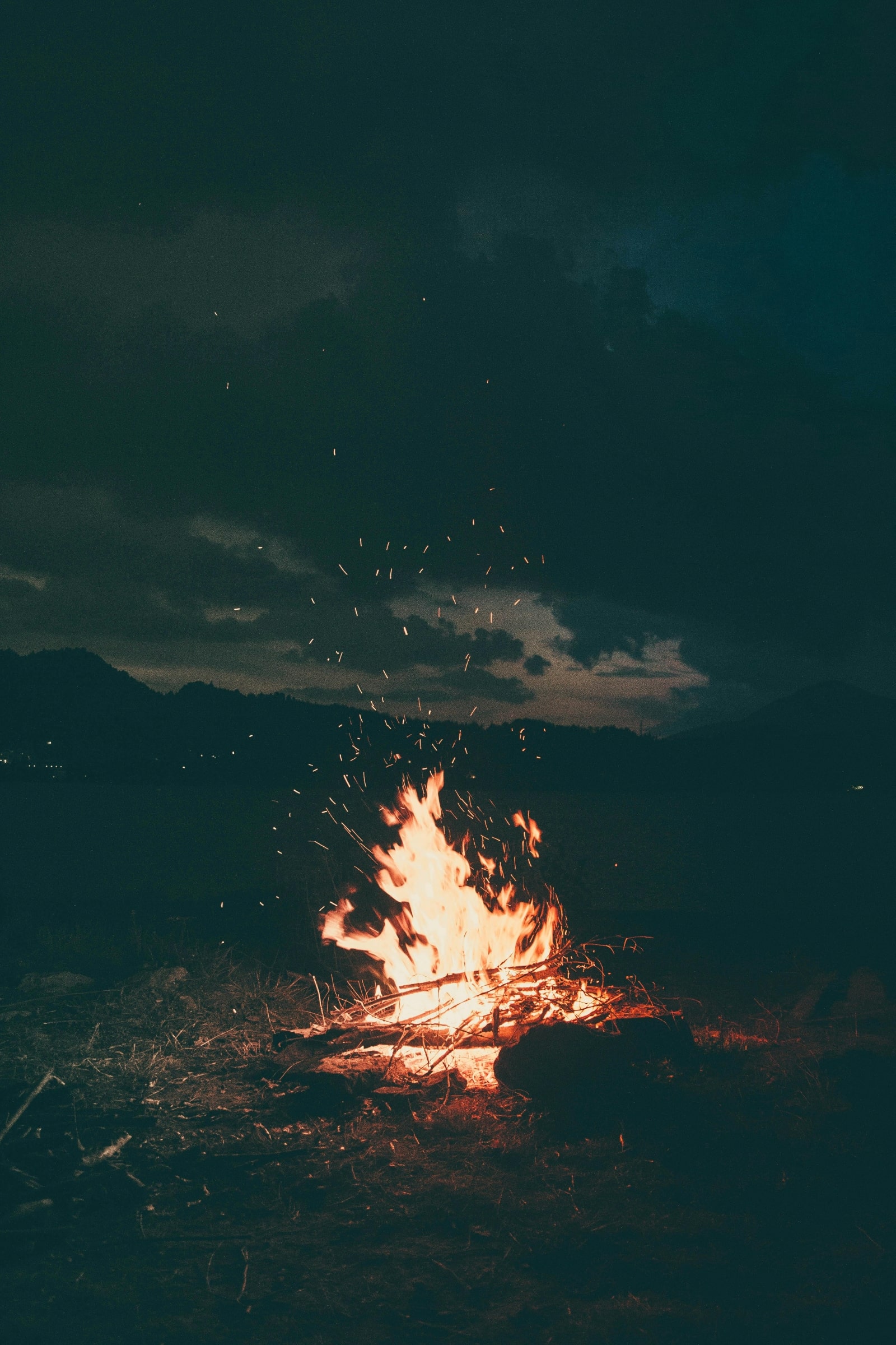 A vibrant bonfire illuminates the beach at night, casting warm light on the sand and surrounding darkness.