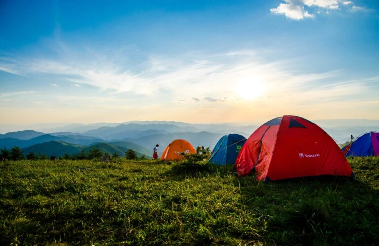 Tents atop a mountain peak as the sun sets, casting warm hues across the sky and illuminating the serene landscape.