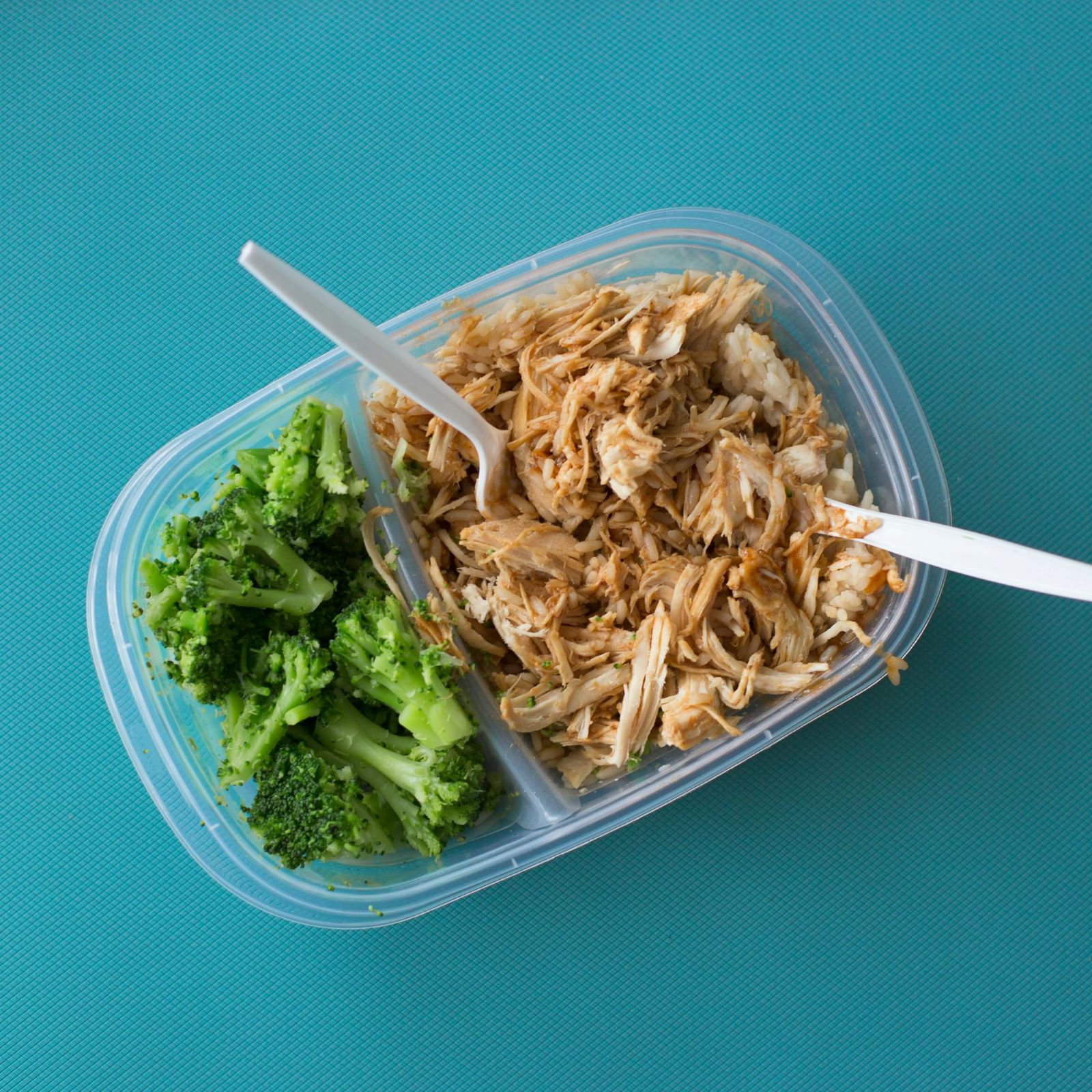 A plastic container filled with cooked broccoli and chicken, showcasing a healthy meal option.