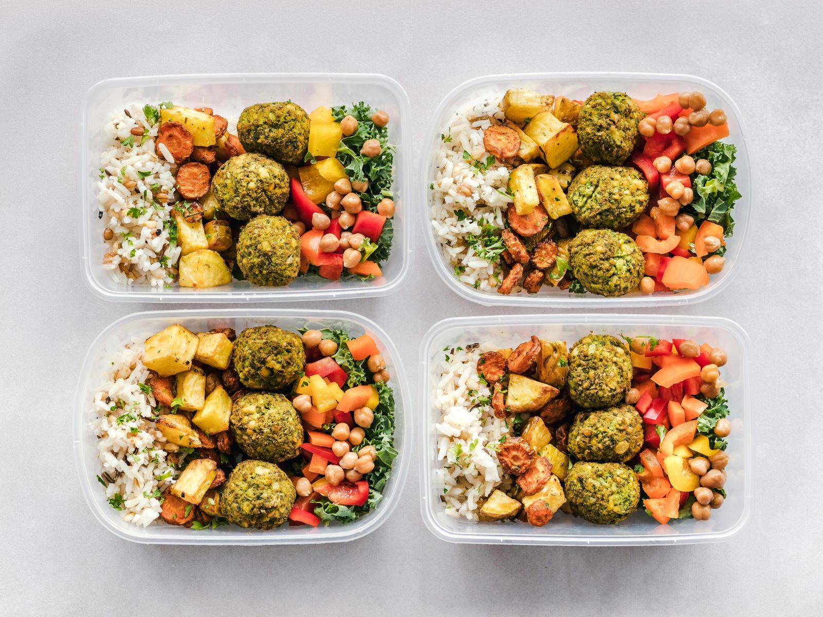 Four plastic containers filled with various types of food arranged neatly on a surface.