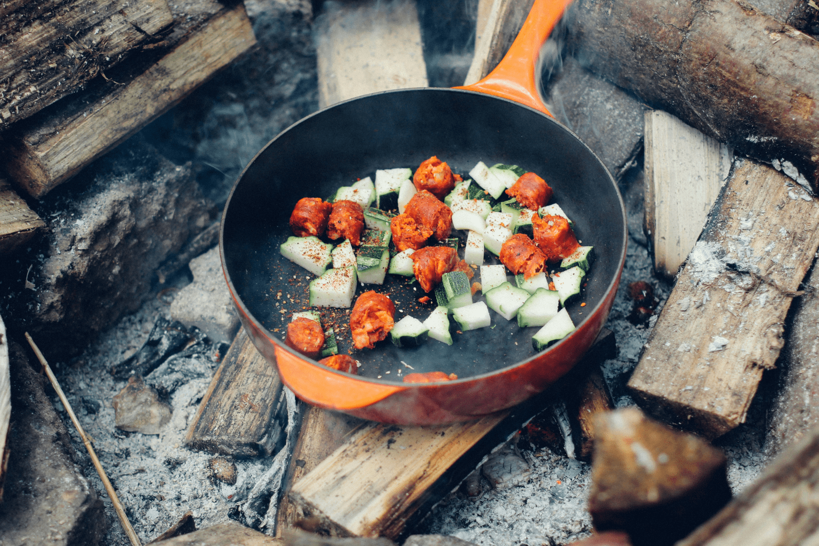 A pan filled with colorful vegetables sizzling over an open fire, showcasing a vibrant cooking scene.