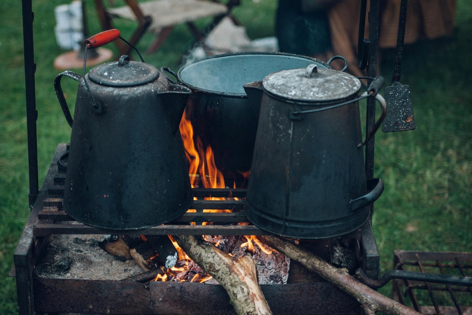 Two pots and a kettle placed over a fire, showcasing a traditional cooking setup in a rustic environment.