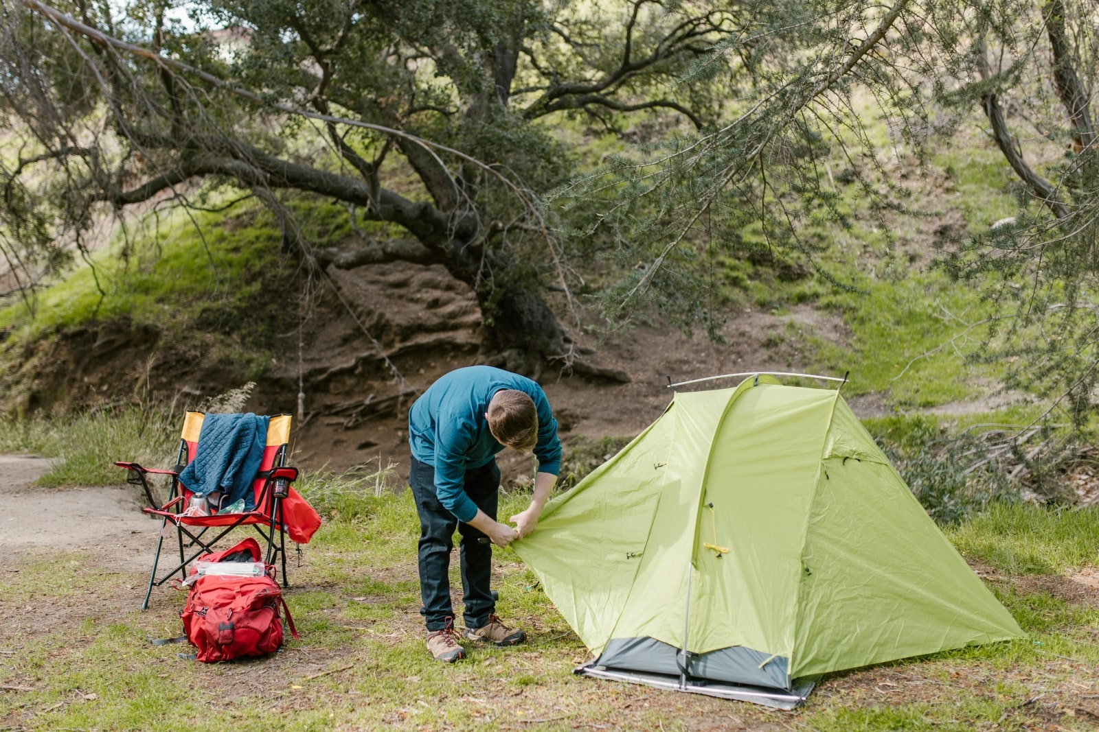 A man is assembling a tent amidst a serene forest setting, surrounded by tall trees and natural greenery.