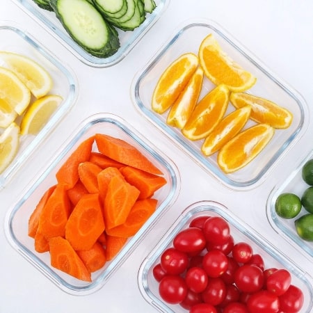 A variety of colorful vegetables displayed in clear containers on a clean white surface.