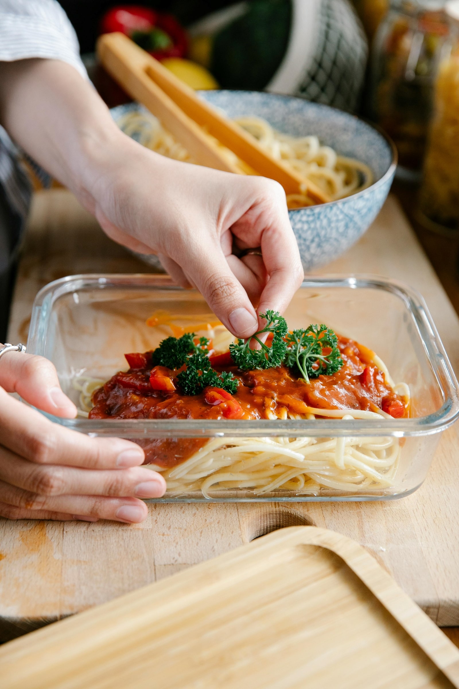 A person carefully places a strand of spaghetti into a dish, preparing a delicious meal.