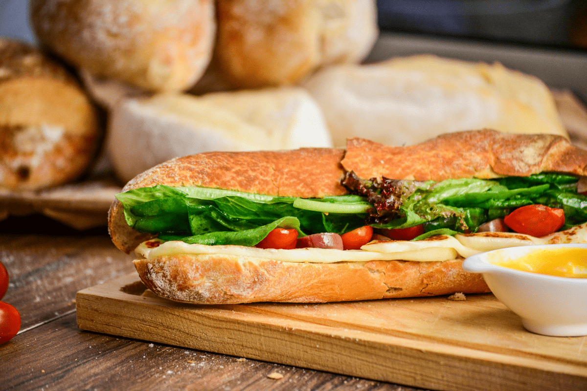 A sandwich with fresh lettuce, ripe tomatoes, and cheese displayed on a rustic wooden cutting board.