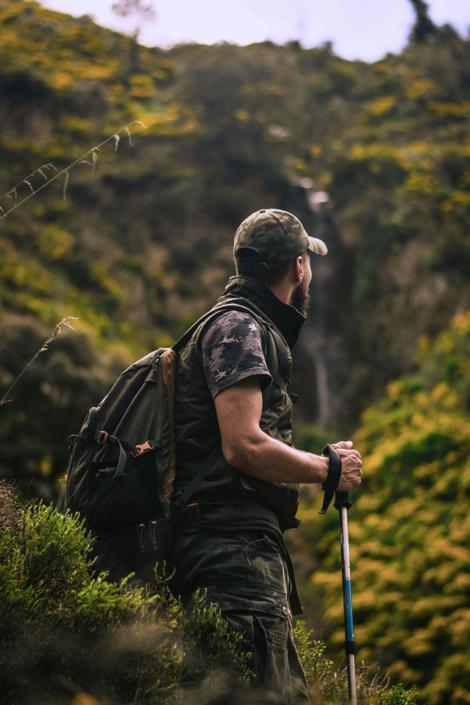 A man stands in a field, equipped with a backpack and hiking poles, ready for an outdoor adventure.