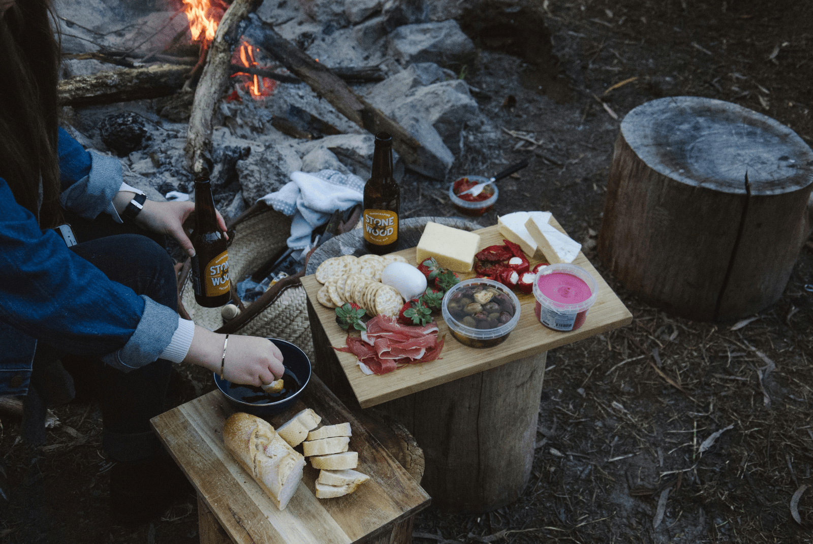 A woman skillfully prepares food over an open fire, surrounded by nature, showcasing her culinary expertise and passion.