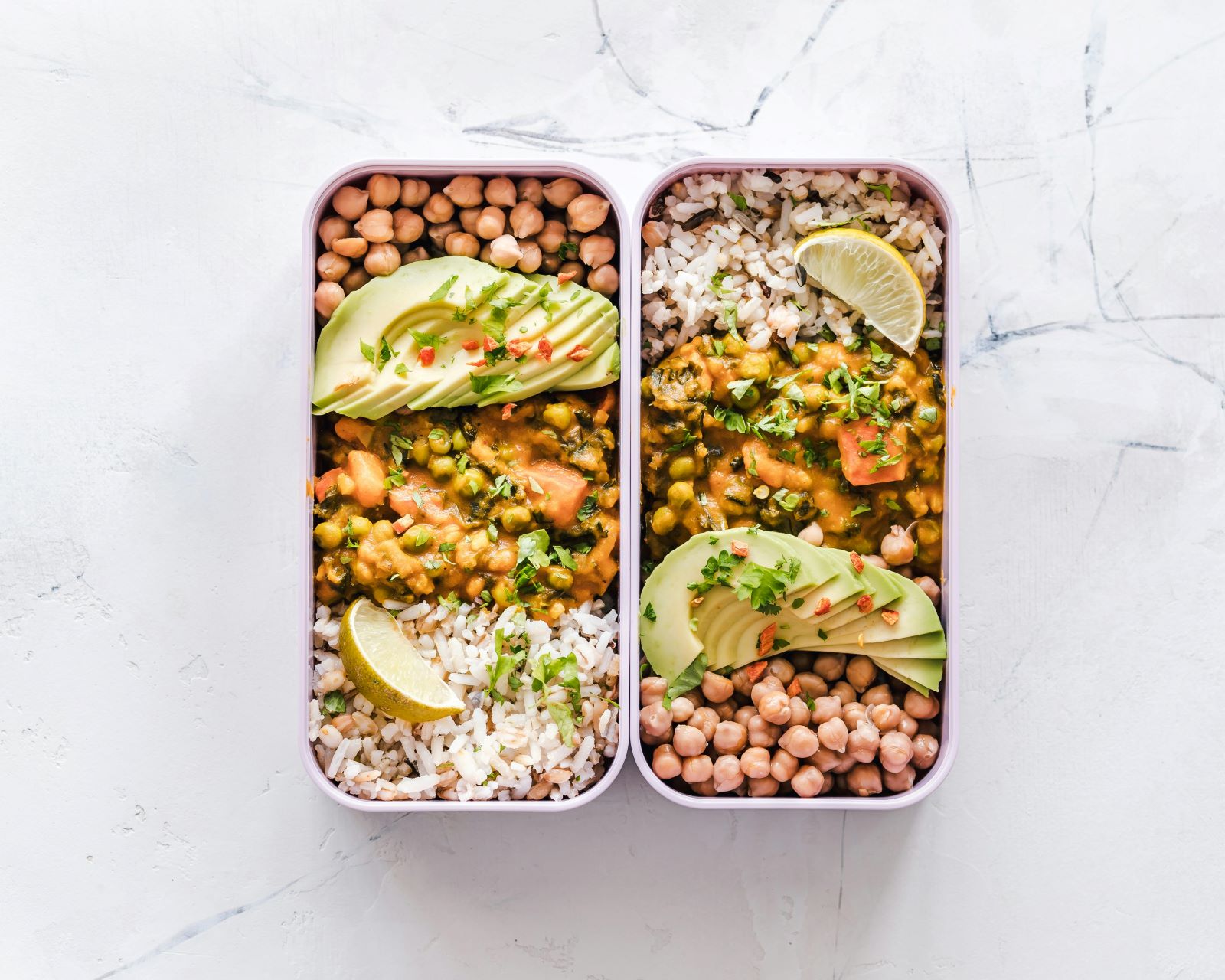 Two lunch boxes filled with rice, beans, and avocado, showcasing a healthy and colorful meal option.