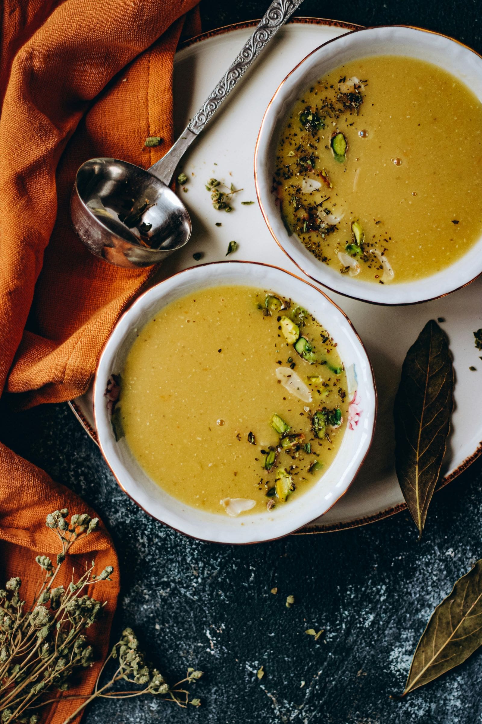 Two bowls of soup with spoons placed beside them, surrounded by leaves on a wooden table.