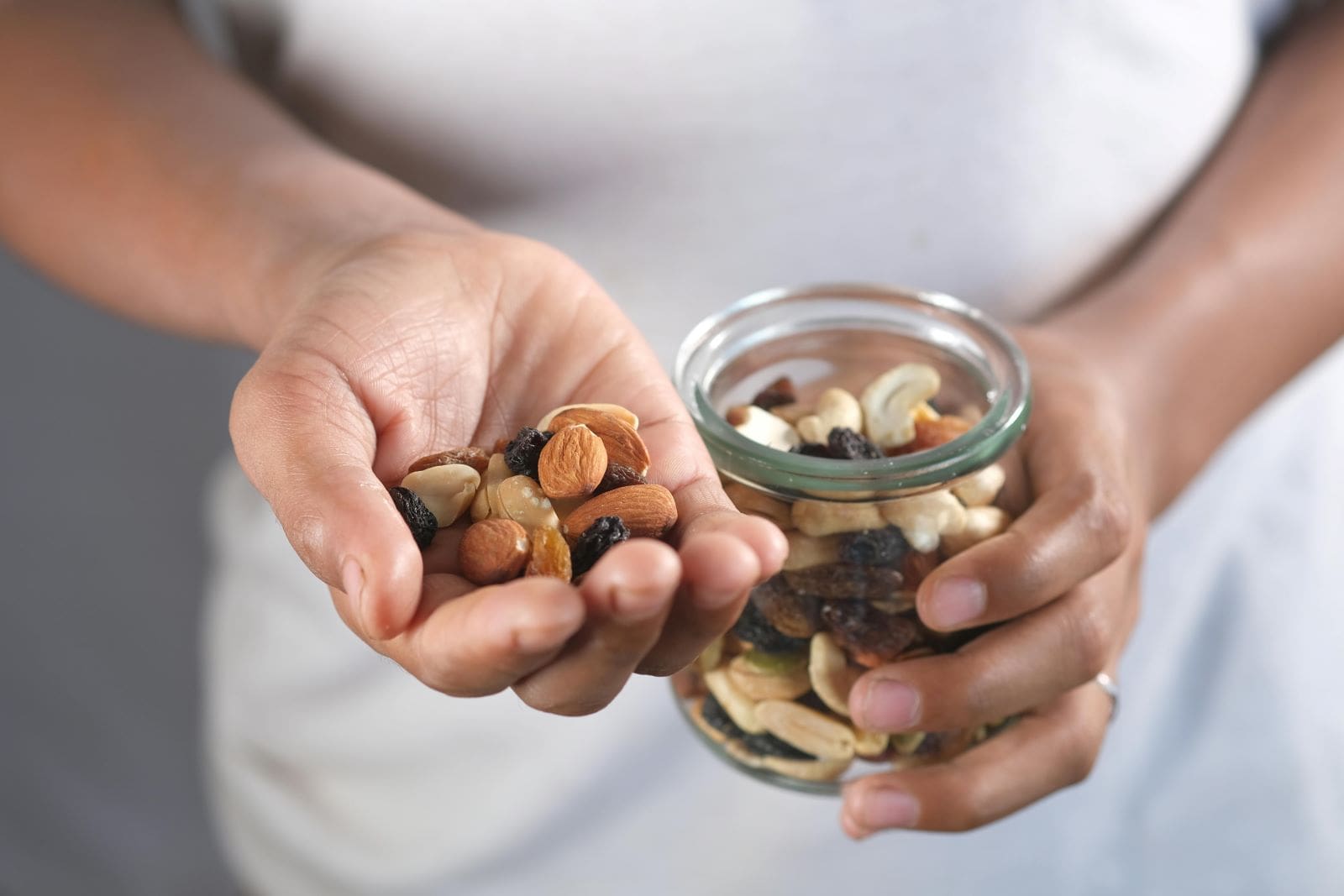 A person holding a jar filled with assorted nuts, surrounded by scattered nuts on a surface.