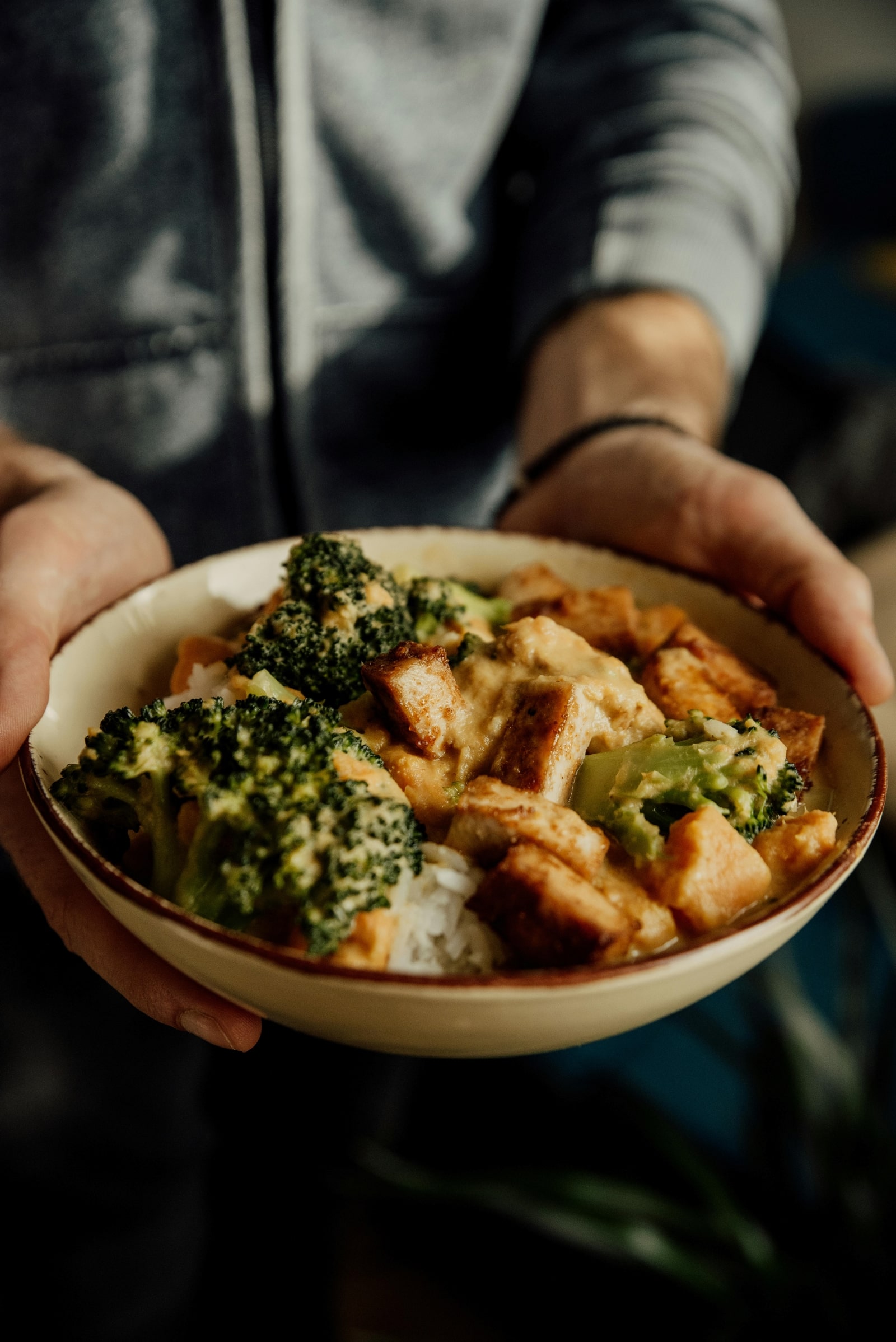 A man holds a bowl filled with broccoli and chicken, showcasing a healthy meal option.