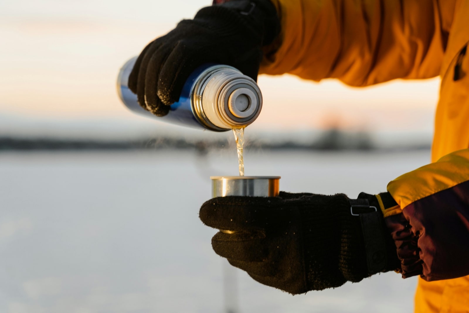 A person dressed in winter attire is pouring a beverage into a cup, showcasing a cozy winter scene.