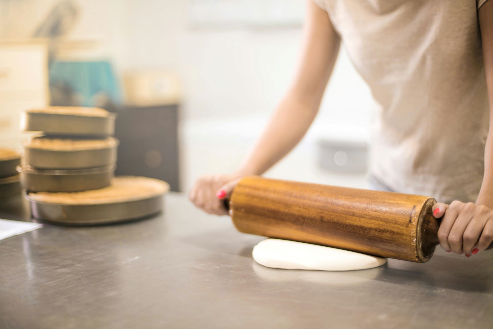 A woman skillfully rolls out dough on a wooden surface using a rolling pin, showcasing her culinary expertise.