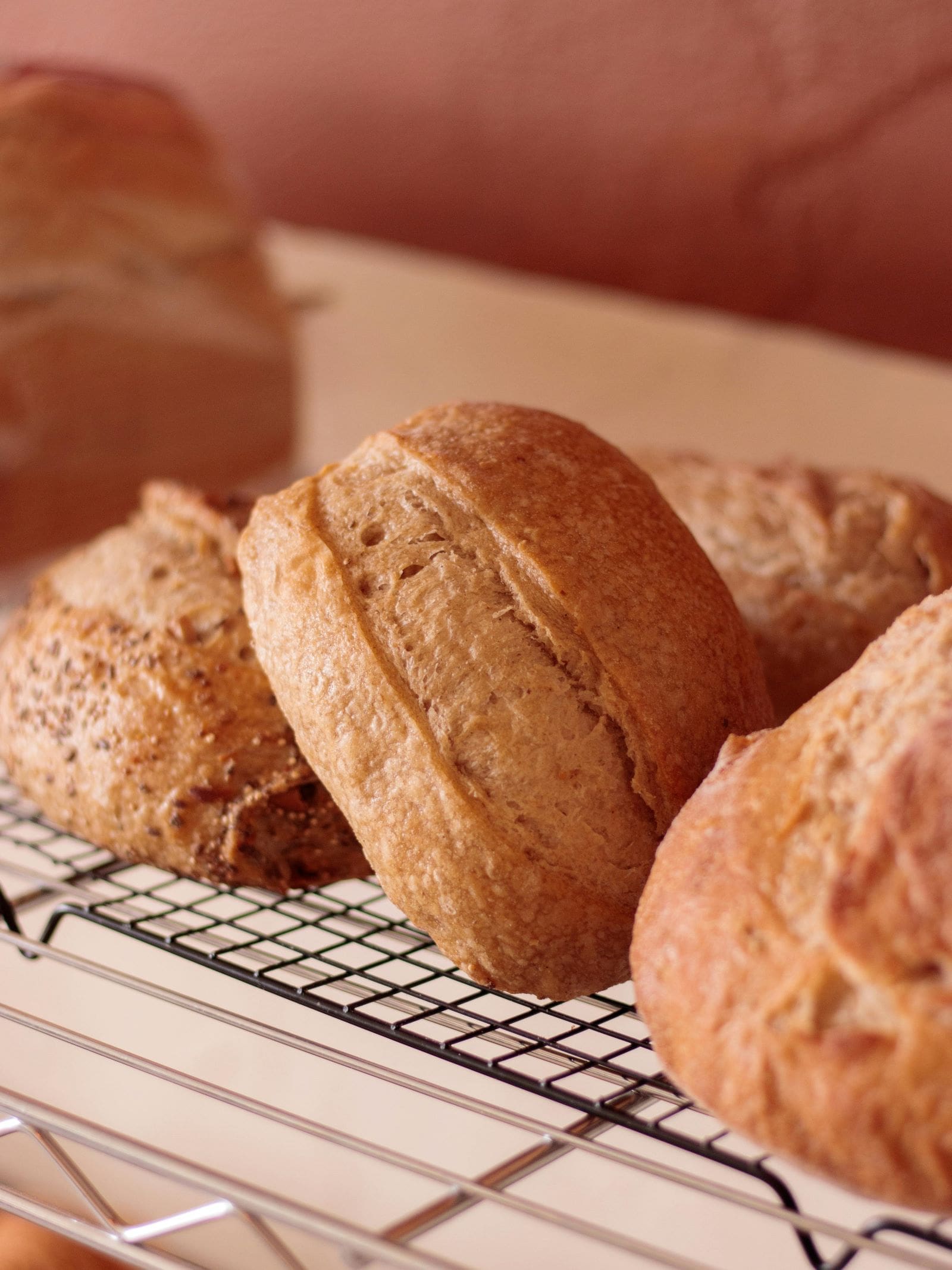 Three freshly baked loaves of bread resting on a cooling rack, showcasing their golden crusts and inviting aroma.