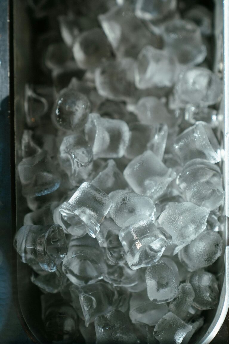 A metal container filled with clear ice cubes, reflecting light and creating a cool, refreshing appearance.