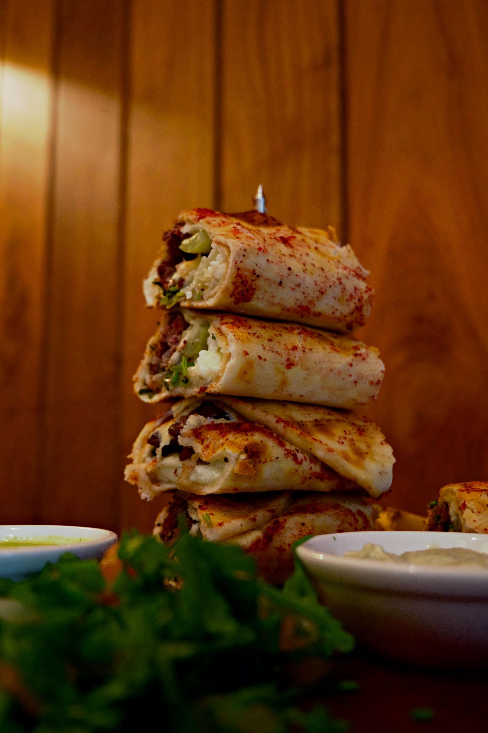 A neatly arranged stack of burritos placed on a wooden table, showcasing their colorful fillings and fresh ingredients.