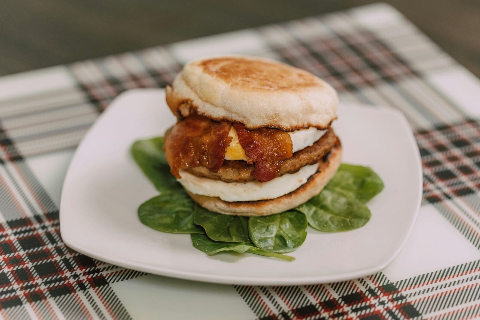 A delicious breakfast sandwich featuring crispy bacon and eggs, elegantly presented on a white plate.