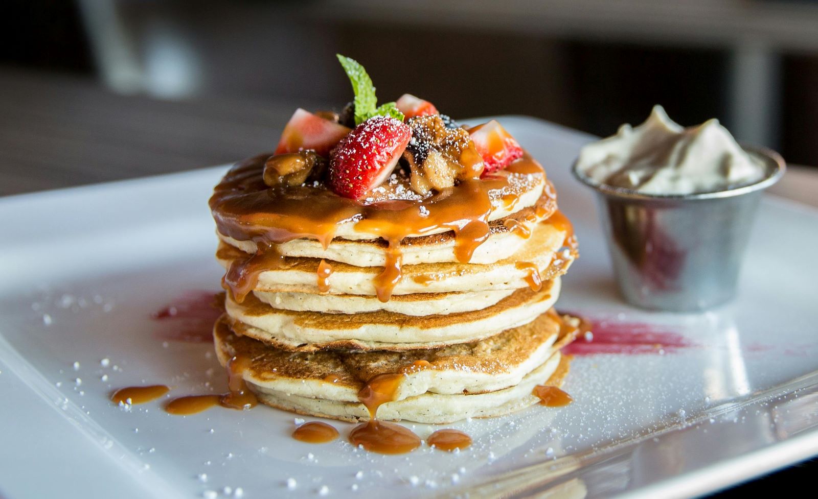 A stack of fluffy pancakes drizzled with syrup and topped with fresh strawberries, creating a delicious breakfast scene.