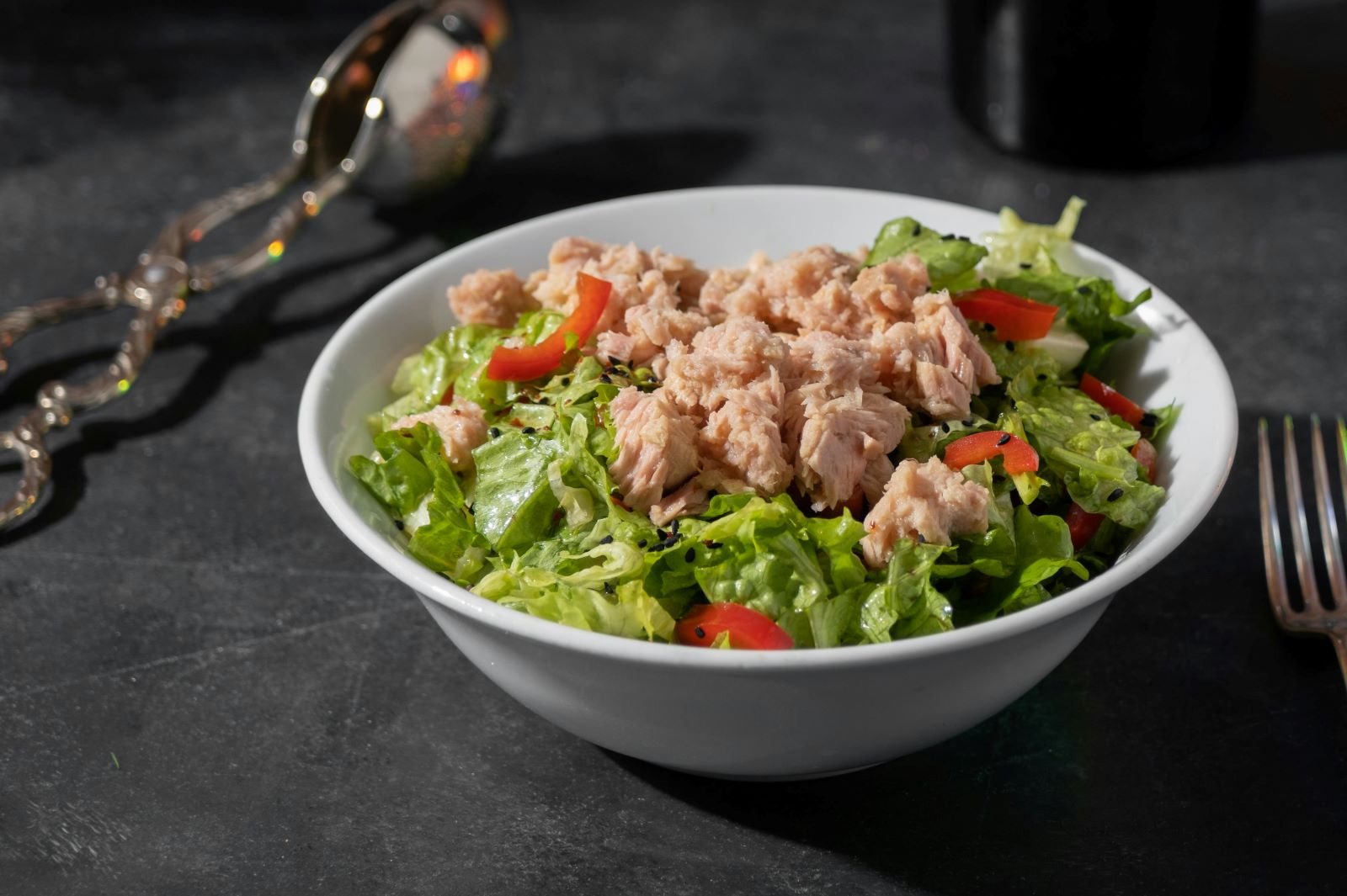 A white bowl filled with a fresh salad featuring tuna and a variety of colorful vegetables.