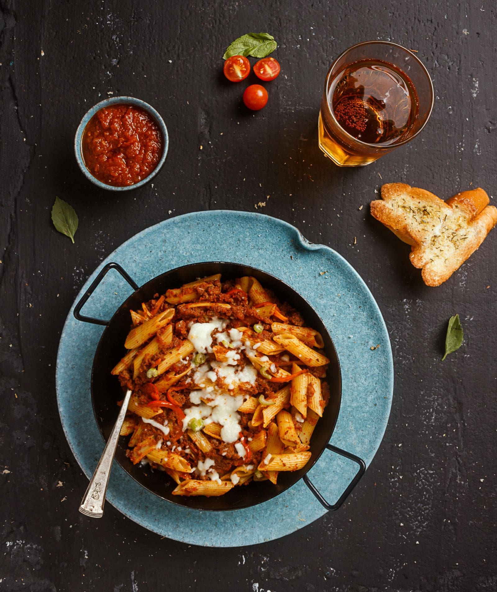 A blue plate holds pasta topped with tomato sauce and cheese, accompanied by bread and extra tomato sauce.