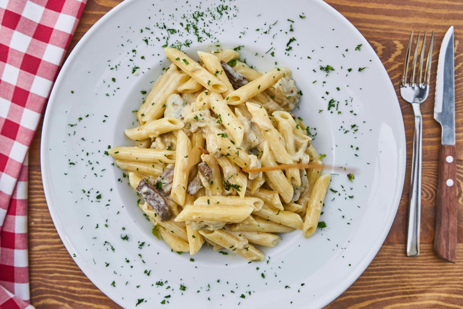 Penne pasta with mushrooms and cheese served on a white plate, placed on a rustic wooden table.