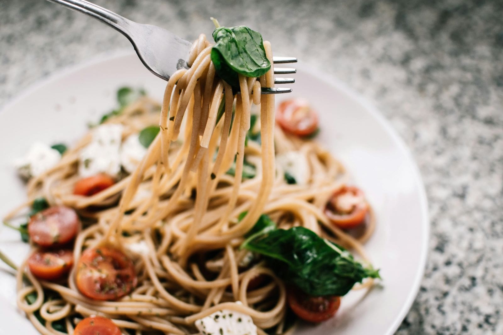 A fork lifts a plate of pasta adorned with fresh tomatoes and vibrant spinach, showcasing a delicious meal.