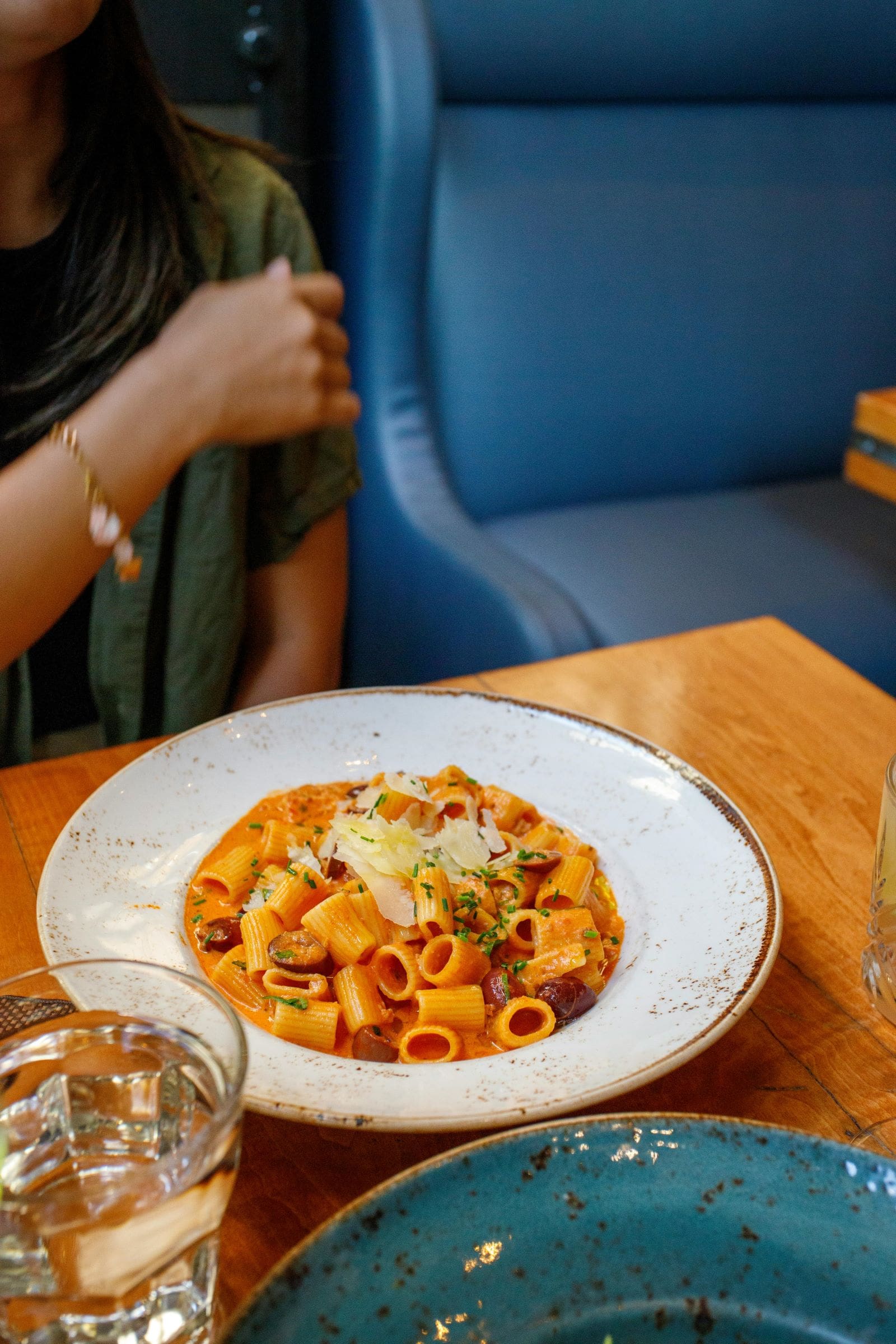 A woman seated at a table, enjoying a plate of pasta in a cozy dining setting.