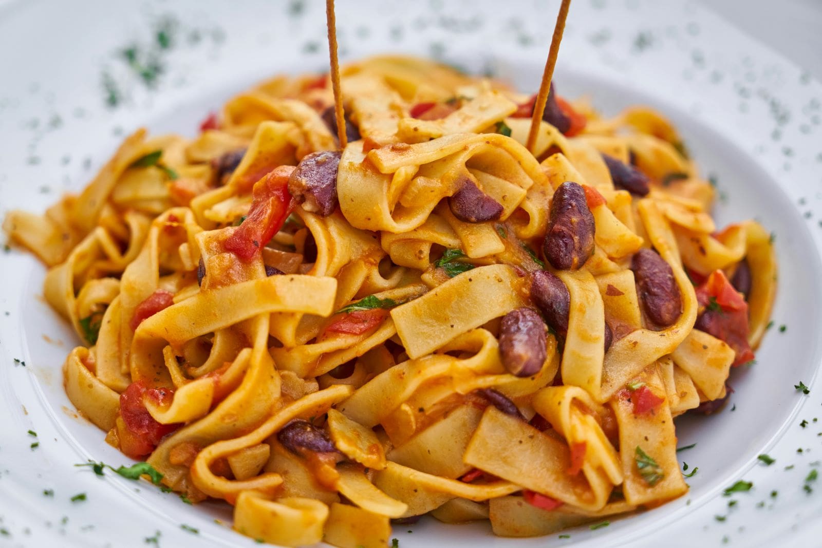 A white plate featuring pasta mixed with beans and tomatoes, showcasing a colorful and appetizing dish.