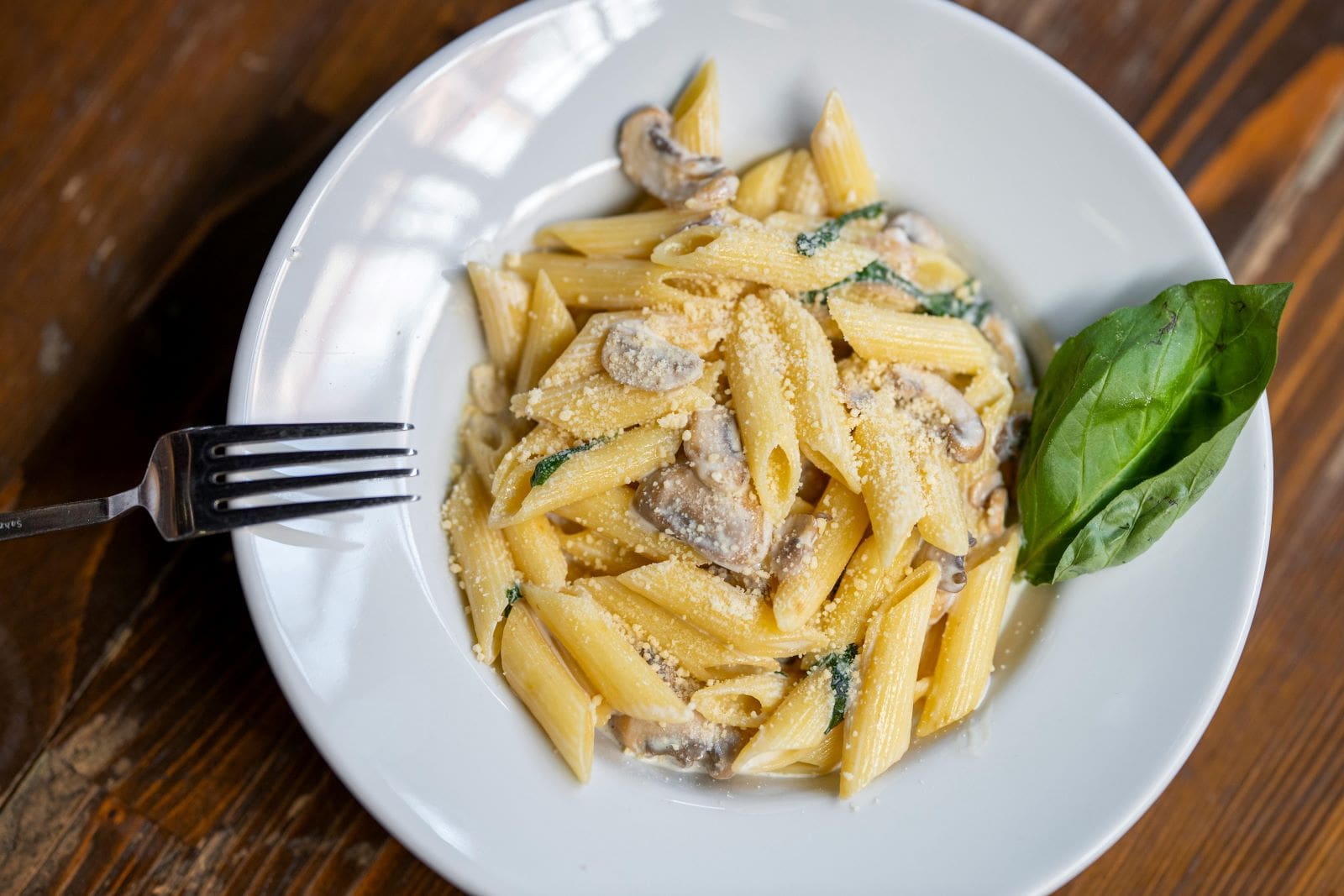 A plate of penne pasta topped with sautéed mushrooms and fresh spinach, garnished with herbs.