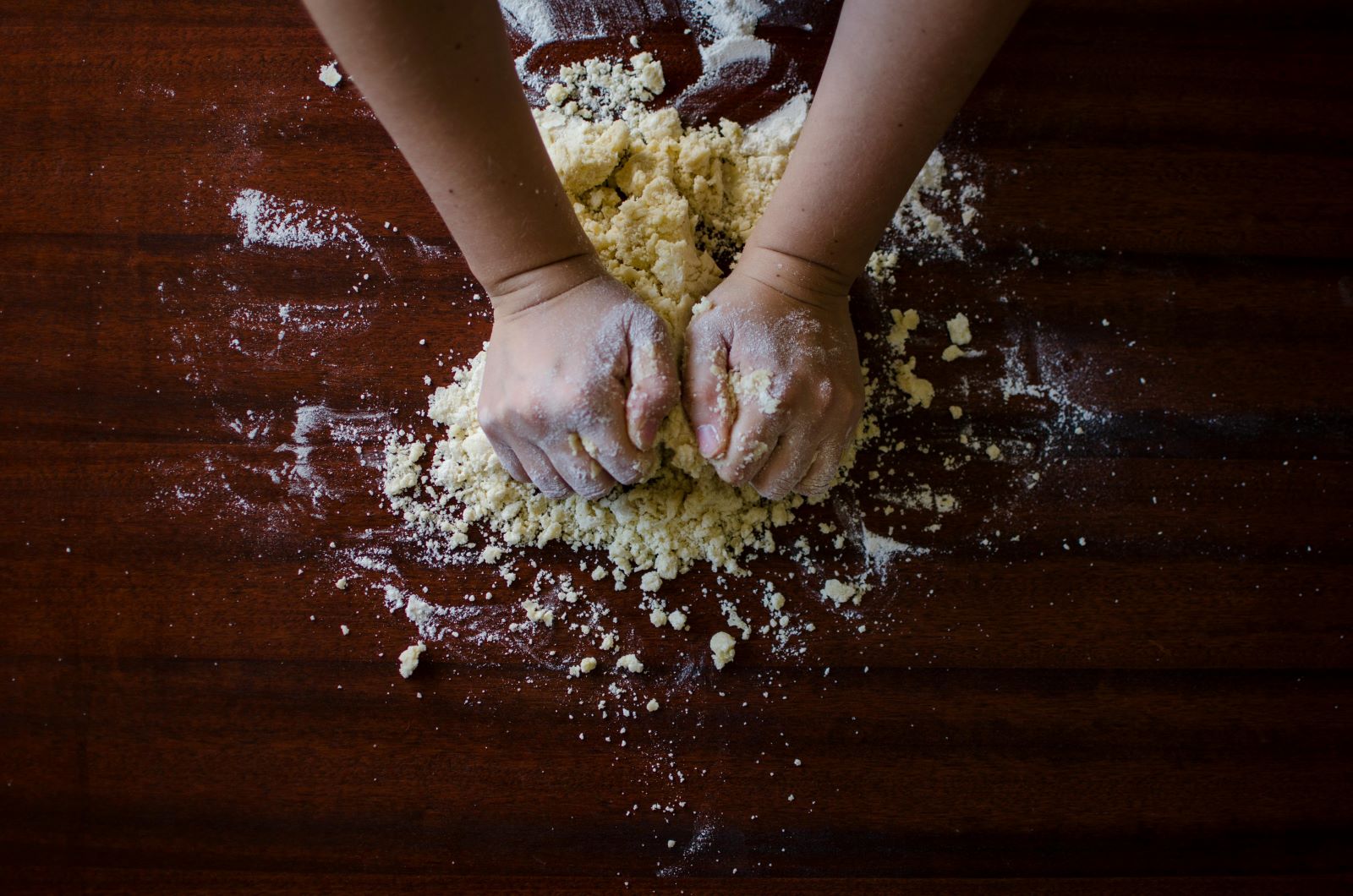 A person's hands skillfully knead dough on a wooden table, showcasing the art of baking and culinary craftsmanship.