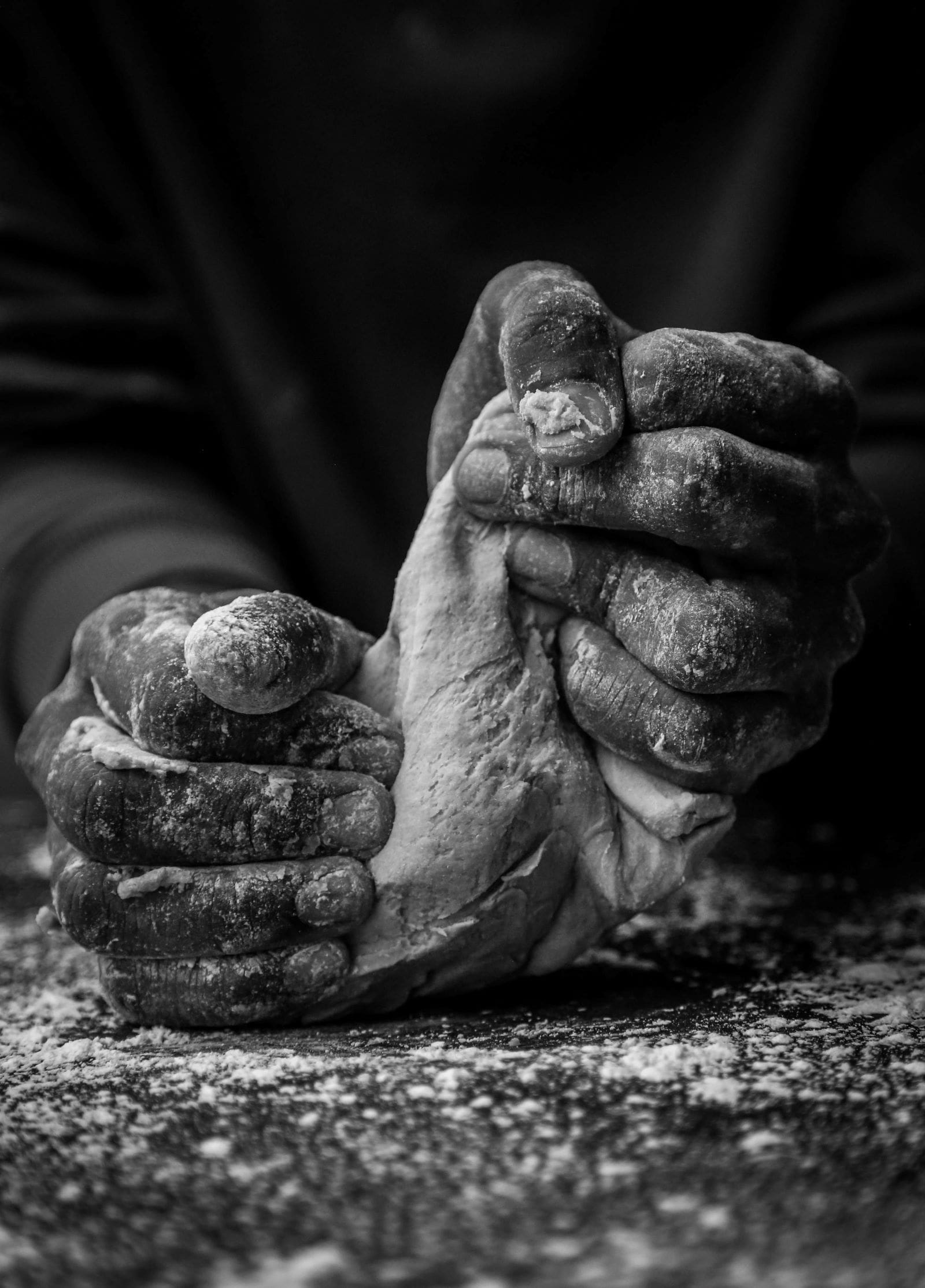 Black and white image of a baker's hands skillfully kneading dough on a wooden surface.